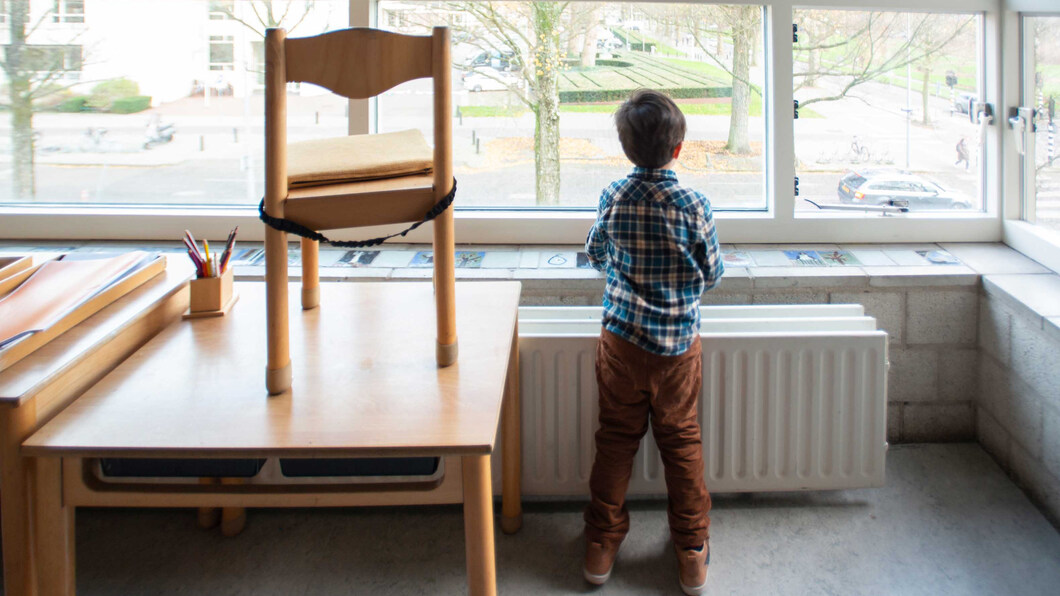 Een kindje staat alleen voor het raam van het klaslokaal naar buiten te kijken