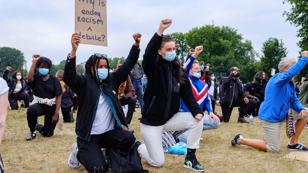 Knielende mensen tijdens een demonstratie tegen racisme. Er is een bord te zien met daarop: why is ending racism a debate?