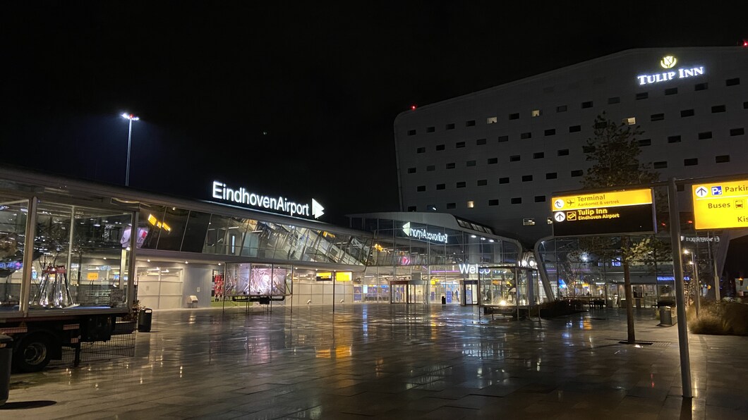 Eindhoven Airport in de nacht. Op de foto staat de aankomstterminal met daarop in lichtgevende letters "Eindhoven Airport".
