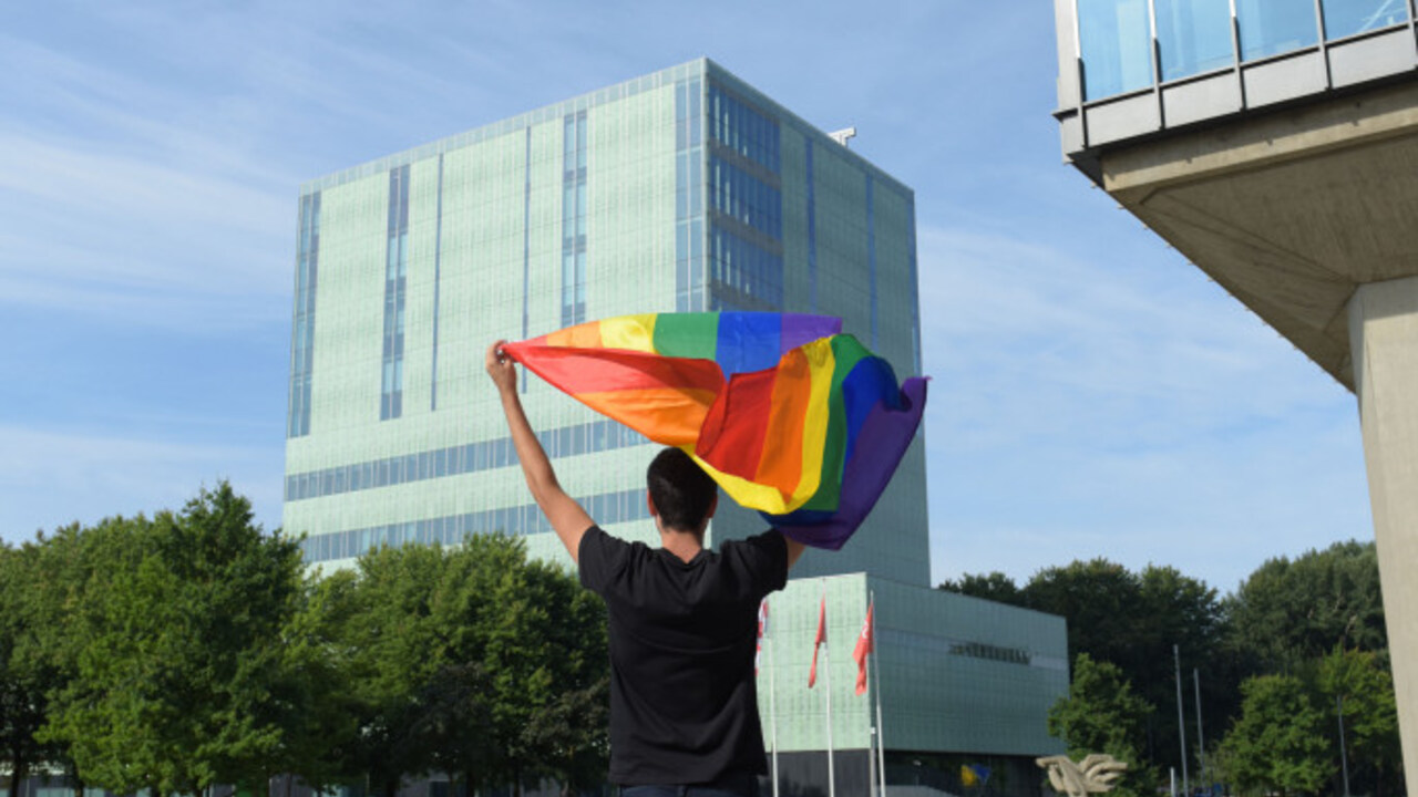 Persoon op TU/e terrein met een regenboogvlag boven het hoofd